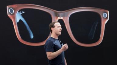 Meta CEO Mark Zuckerberg on a stage describing Meta's Ray-Bans, a large image of which is being shown behind him.