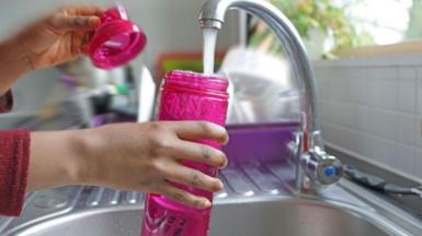 Person filling up a pink bottle with water at a kitchen sink