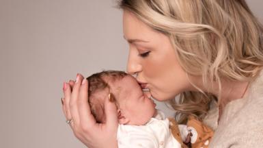 Laura Hudson kisses her newborn daughter Aurora on her forehead while cradling her in her arms.