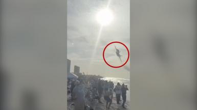 Jet flying above a crowd on a beach with a red circle around it.