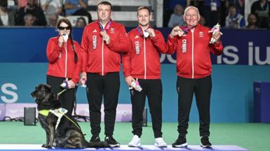 Para bowlers Julie Thomas and Steffan James receive their medals alongside directors John Wilson and Jamie Jones with Julie’s guide dog Yoko.