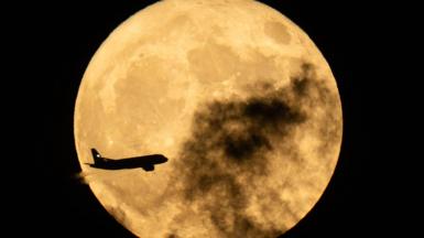 A plane seen flying in front of a Flower Moon