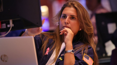 Female stock market trader in blue jacket with American flag looks at computer screen