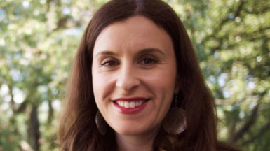 A woman with long dark hair and big earrings smiles at the camera.