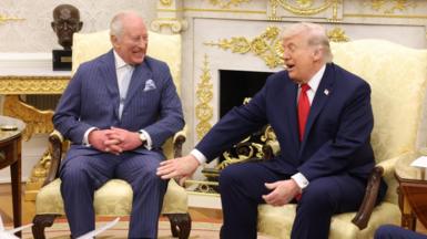 King Charles III and US President Donald Trump smile as they sit side by side on chairs in the Oval Office