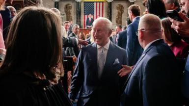 King Charles, with a grin on his face, walks by lawmakers in US Congress after delivering his speech, with US Vice-President JD Vance and a US flag visible distantly behind him