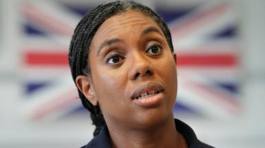 Kemi Badenoch speaking, with a blurred Union Jack in the background