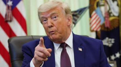Donald Trump sits in a leather chair in the Oval Office and points his index finger while speaking