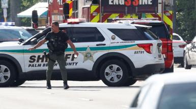 A police officer gestures in front of a sheriff's vehicle and a fire engine, with other cars to the right of frame, in West Palm Beach, Florida, U.S. September 15,