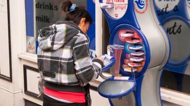 A woman fills out a form for a National Lottery ticket at a stand outside a shop