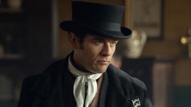 James Norton in character as Sean Rafferty wearing a black top hat and white scarf 