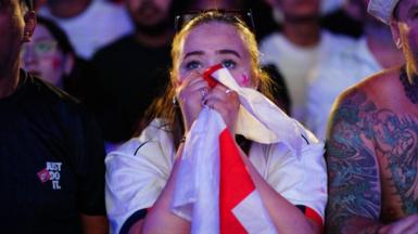 Woman holding England flag to her face looking shocked