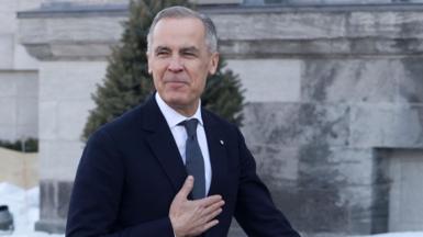 Mark Carney walking along with his hand on his heart.