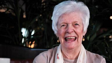 Marie McLaren smiles for the camera. She has short grey hair and is wearing a white scarf.