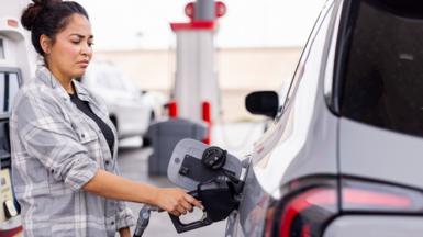 Woman fills silver car at US gas station