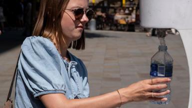 People using a water fountain to top up their water bottles in the Spring heat to keep cool and hydrated during the first heatwave of the year
