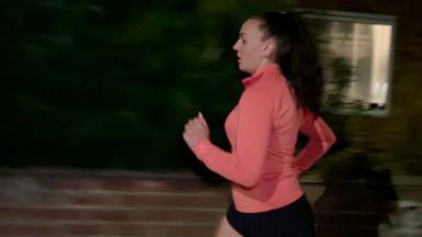 Natalie Bell runs past a house in the dark. She is wearing a pink running top and black shorts.