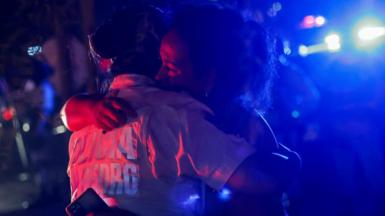 Two people hug, illuminated by red and blue lights