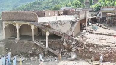 Debris from a partially destroyed home falls from a bank carved in the earth from flood waters.