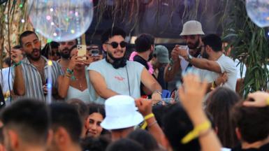 People DJ, dance and take video in a crowd at a Syrian electronic music concert