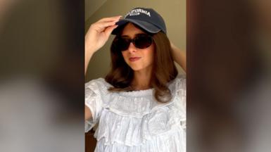 A young woman wearing a white top, sunglasses and a navy cap.