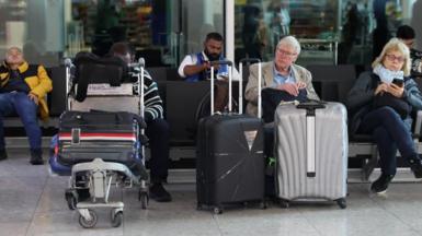 People sit inside an airport with their luggage.
