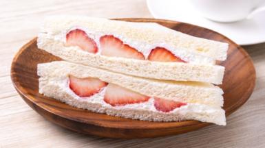 A strawberry and cream sandwich in white bread, served on a wooden plate on top of a table