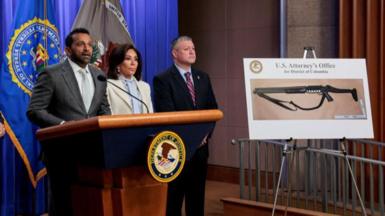 Prosecutors announce charges standing next to an image of the suspect's shotgun