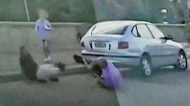 Still from a grainy dashcam video showing two men grappling with a gun. One is dressed in black, the other in purple