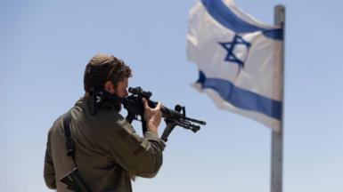 An soldier with a gun stands near an Israeli flag