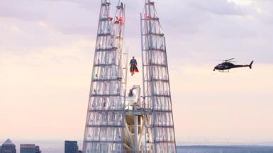 A figure of superman is suspended at the peak of the shard. A helicopter is hovering behind.  