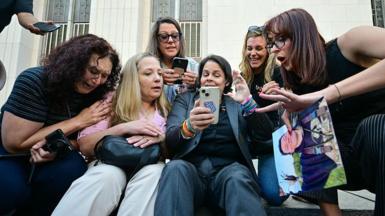 A group of women sit on steps in front of an Los Angeles courthouse and react with happiness and tears at verdict 