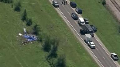 A view of the crash site on the left with vehicles parked along the road to the right