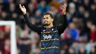Iliman Ndiaye wears a black jersey with blue and yellow zig-zag stripes. His arms are raised in celebration after scoring a goal.