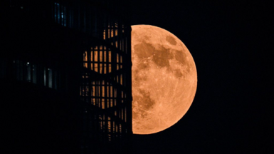 A bright moon partly obscured by a building