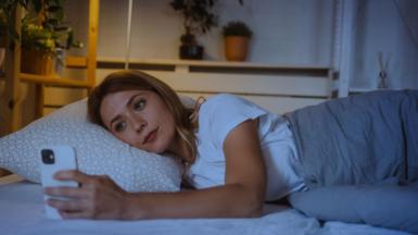 Woman lies in bed at night looking at her smartphone