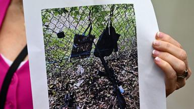 A printed photo held up by a person wearing a pink top shows the rifle and other items, that look like bags hanging on a fence, found near where a suspect was discovered during a press conference regarding an apparent assassination attempt of former President Donald Trump on September 15, 2024, in West Palm Beach