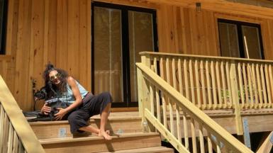 Wearing sunglasses and holding her black dog, Erica Cirino sits on the wooden steps of her home. 