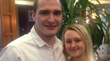 Smiling Chris Taylor, who has brown hair and a beard and is wearing a white shirt, is pictured with his partner Jemma, who has long blonde hair and minimal make-up, in the foyer of a venue