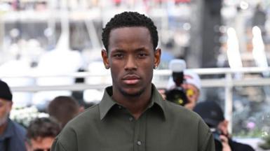 Ward looks straight at the camera at an event. He is wearing a green collared shirt and is wearing an earring.