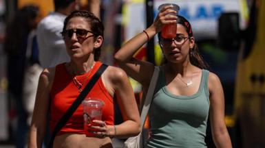A woman cools her head with an iced drink as she walks through central London on a sunny day.