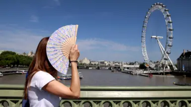 Woman fans herself on a hot sunny day in London with the London Eye in the background