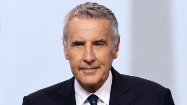 Dermot Murnaghan, who has grey hair, looks slightly off camera while wearing a suit.