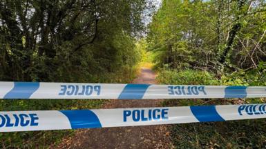 police tape in blue and white over a footpath in Wakefield with trees on either side 