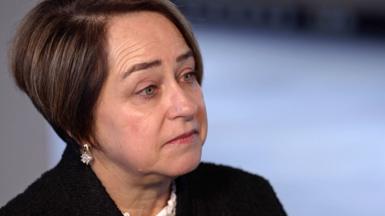 Mandy has short dark hair, is wearing a dark textured jacket and small drop earrings, and is turned slightly to one side with the face in profile.