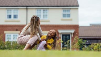 A mother plays with her daughter in a park in front of housing in the North East of England