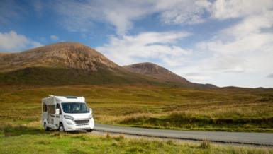 A white campervan parked next to a narrow road in front of a mountain