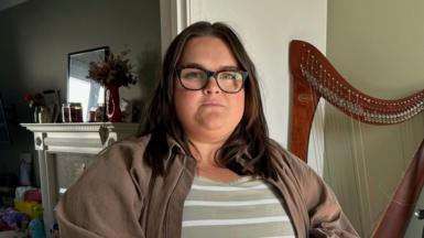 Gabriella Smith - she has long dark hair and glasses. She wears a striped top with a brown jacket over the top.