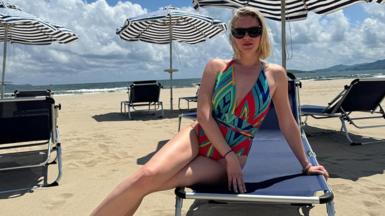 Anastasia Samsonova, with blonde hair and a multi-coloured swimsuit, relaxing on a sun lounger on a deserted beach at Wonsan Kalma