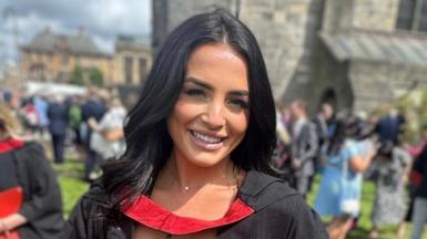 Louise Fraser at her graduation. She has long, black hair and is wearing a black and red graduation gown. There are people in the background who have been blurred.